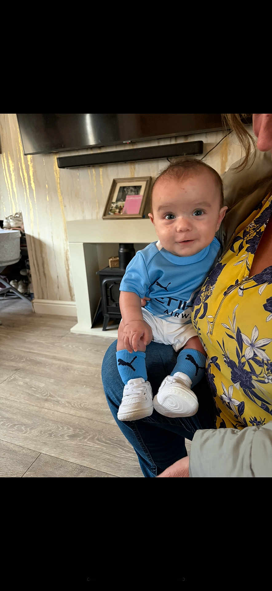 Riko joined the competition — help win amazing prizes! baby, child, infant, blue_clothing, socks, white_shoes, adult, floral_top, living_room, fireplace, wooden_floor, portrait, smiling, person, home_interior, casual, seated, indoor, cute, holding