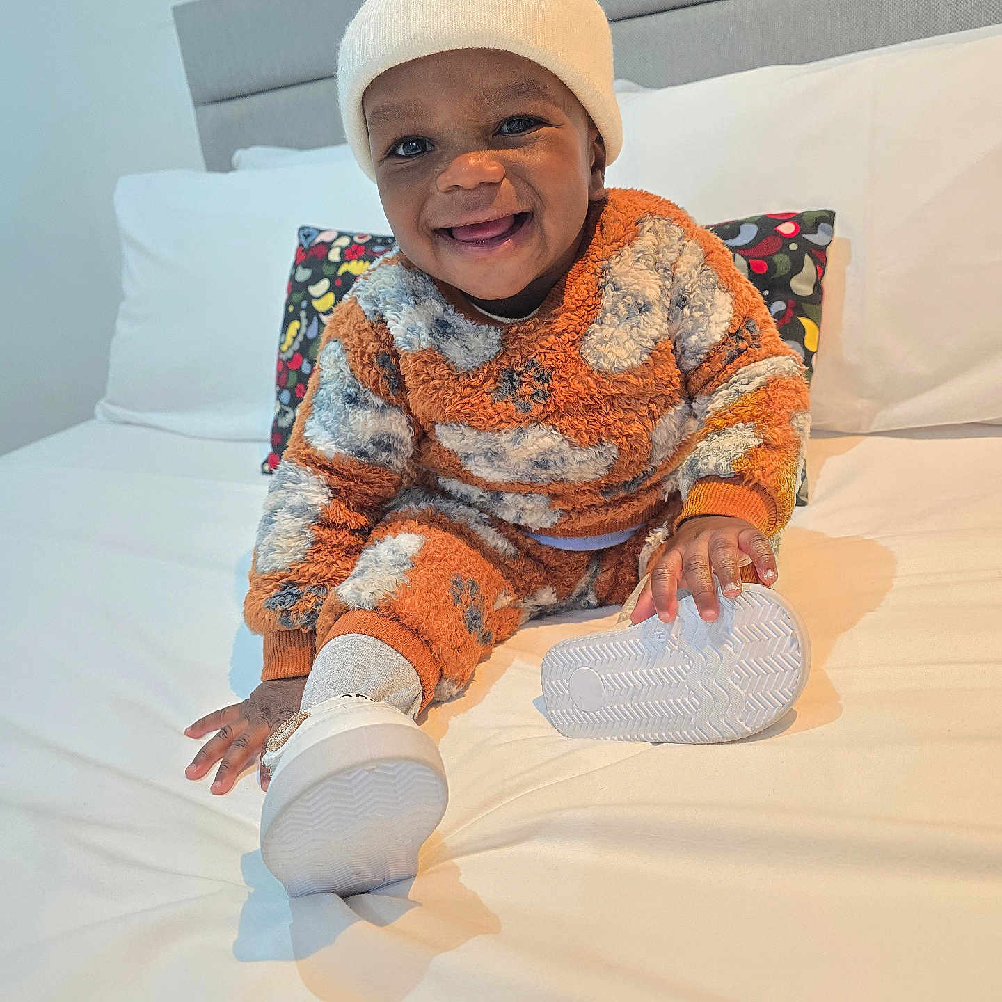 Naheem joined the competition — help win amazing prizes! beanie, bed, child, cute, expression, footwear, fuzzy_outfit, happy, headwear, indoor, orange_clothing, person, pillow, playful, portrait, sitting, skin, smiling, toddler, white_shoes