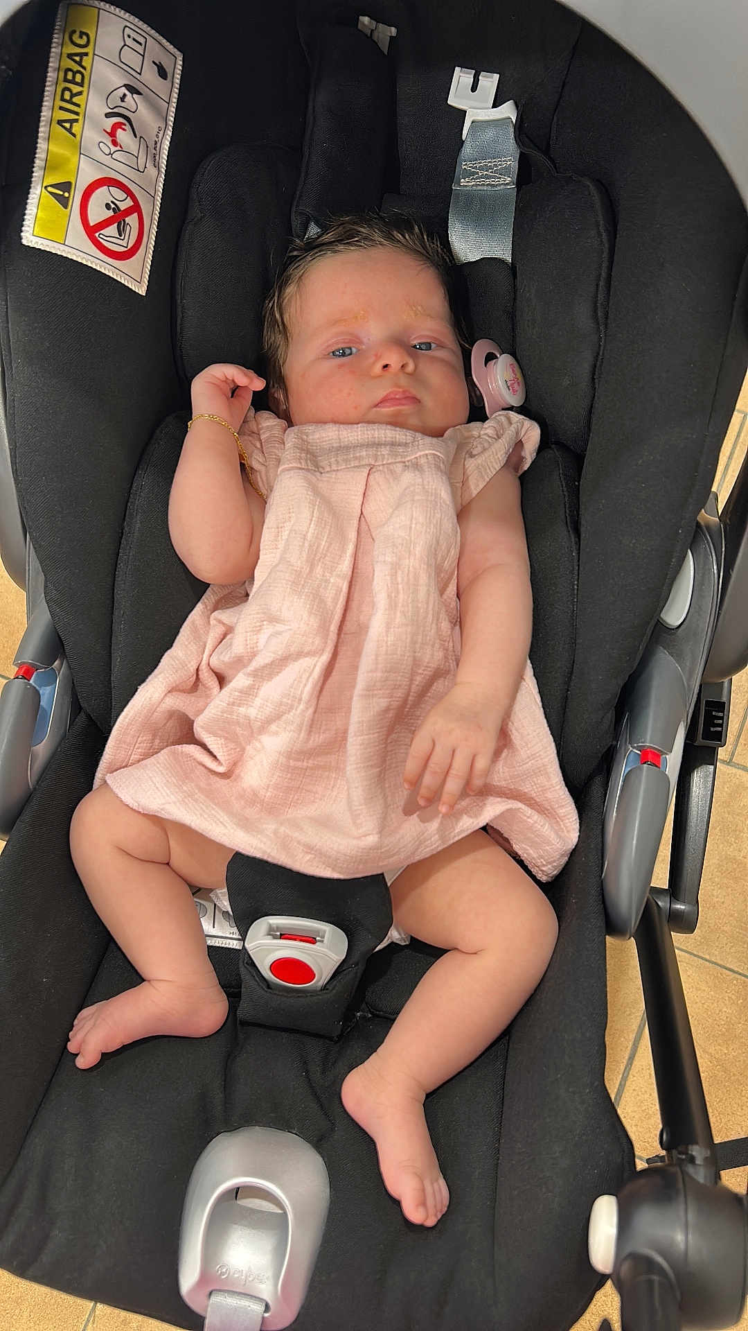 Jade a rejoint le concours — aidez-le/la à gagner de superbes lots ! baby, infant, car_seat, pink_dress, pacifier, bracelet, footwear, child, seatbelt, indoor, floor_tiles, black_fabric, cute, person, newborn, resting, portrait, skin, hand, foot