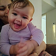 Harmony is registered to the contest to win money with this photo: baby, smile, tongue_out, infant, person, adult, hand, clothing, long_sleeve, floral_pants, indoor, wall, door, happy, holding, face, portrait, cute, child, family