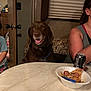 dog, brown_dog, table, food, plate, soda_can, person, child, indoor, seated, smiling_dog, furniture, window_blinds, couch, happy, meal, family, casual, relaxed, domestic