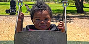 Miles is registered to the contest to win money with this photo: black_swing, blue_sky, chains, child, curly_hair, daytime, fun, grass, happy, nature, outdoor, park, person, play, playground, smiling, sunny, swing, toddler, trees