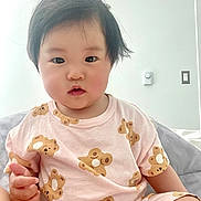 Iris joined the competition — help win amazing prizes! toddler, child, baby, pink_clothing, teddy_bear_pattern, short_sleeves, indoor, white_wall, light_switch, thermostat, bed, blanket, black_hair, curly_hair, cute, portrait, sitting, hand, face, innocent_expression