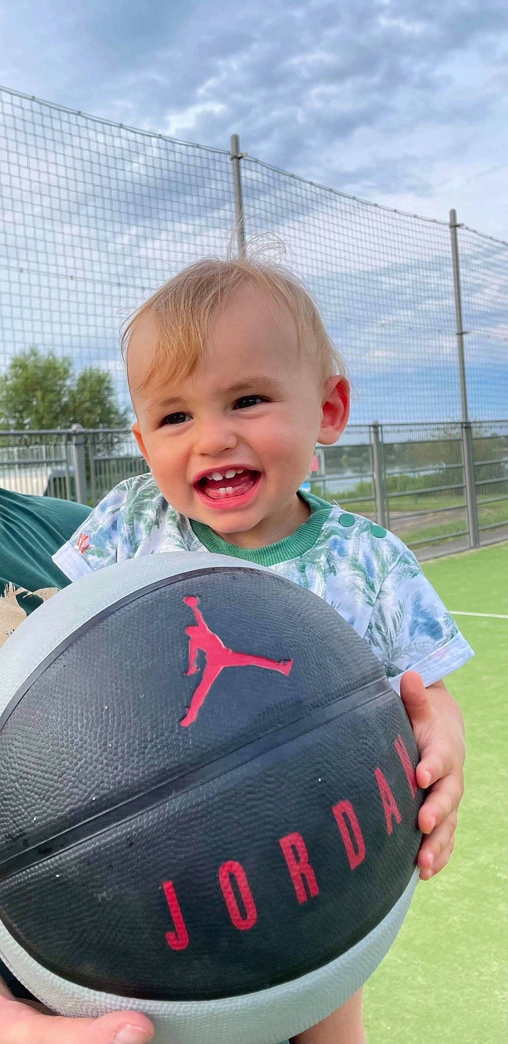 Leno participe au concours pour gagner de l'argent avec cette photo : automotive_exterior, ball, baseball_protective_gear, child, cloud, fence, fun, grass, happy, leisure, person, personal_protective_equipment, recreation, sitting, sky, smile, sports_equipment, sports_gear, t_shirt, toddler