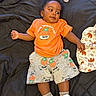 Prince joined the competition — help win amazing prizes! baby, child, orange_shirt, shorts, skateboard_print, black_blanket, toy, bottle, animal_print_blanket, sneakers, socks, curly_hair, lying_down, indoor, cute, playful, infant, clothing, footwear, expression