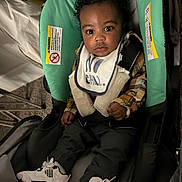Prince joined the competition — help win amazing prizes! baby, child, car_seat, sneakers, bib, plaid_shirt, clothing, person, indoor, seat_belt, infant, footwear, curly_hair, looking, portrait, cute, expression, carrying_device, fabric, small_child