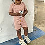 toddler, child, pink_outfit, shorts, sneakers, white_wall, parking_garage, concrete_floor, standing, curious, urban, clothing, person, footwear, casual, young_child, holding_object, braided_hair, expression, indoor
