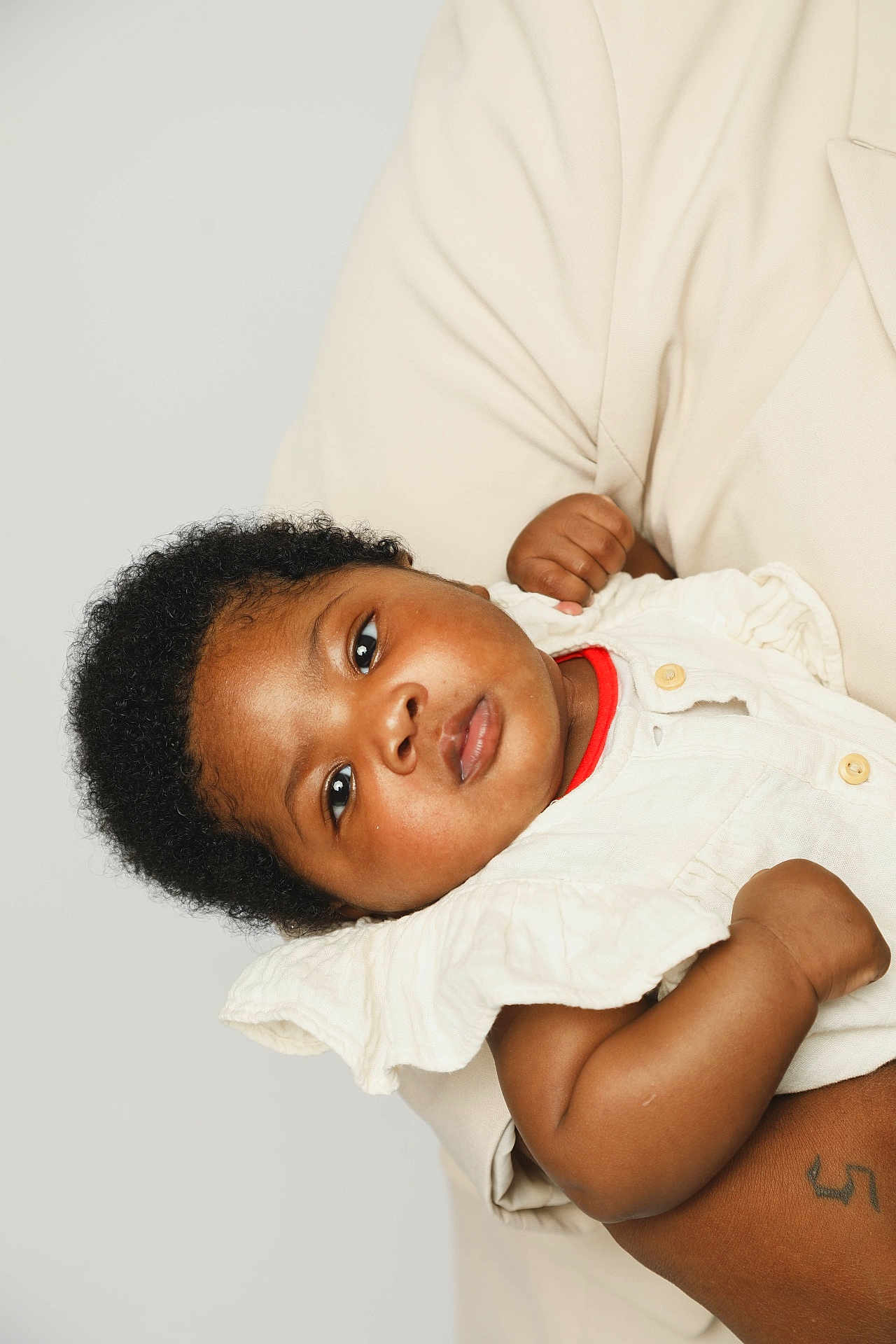 Kaylee participe au concours pour gagner de l'argent avec cette photo : baby, child, curly_hair, infant, person, portrait, clothing, white_outfit, red_collar, arm, tattoo, skin, hand, adult, holding, closeup, expression, face, gaze, soft_light