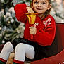 child, girl, red_sweater, bell, holiday, christmas_tree, festive, smile, white_tights, colorful_socks, wooden_crate, indoor, holiday_decor, joyful, portrait, cute, holiday_spirit, seasonal, celebration, young_child