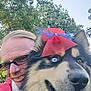 person, dog, outdoor, smiling, glasses, bow, canine, face, happy, tongue_out, pet, nature, tree, sunlight, close_up, heterochromia, fur, friendship, park, leisure