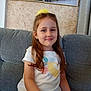 child, girl, smiling, sitting, couch, white_tshirt, yellow_shorts, hair_accessory, indoor, portrait, happy, wall_art, painting, home_interior, curtain, furniture, casual_clothing, young, person, relaxed