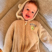 Elijah joined the competition — help win amazing prizes! child, baby, toddler, smile, hooded_jumpsuit, fuzzy_texture, pooh, couch, sofa, fabric, happy, teeth, blue_eyes, rosy_cheeks, zipper, lying_down, home_interior, cozy, playful, hood