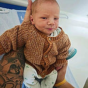 Tymëo a rejoint le concours — aidez-le/la à gagner de superbes lots ! baby, infant, knitted_sweater, tattoo, hand, person, clothing, blue_towel, white_background, cute, newborn, portrait, holding, expression, sitting, cozy, cute_face, small_hands, patterned_pants, indoor