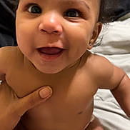 Brooklynn is registered to the contest to win money with this photo: baby, smiling, curly_hair, dimples, bare_chest, hand, blanket, diaper, infant, cute, happy, person, skin, indoors, closeup, child, joyful, holding, soft, young
