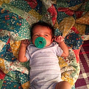 Danielle is registered to the contest to win money with this photo: baby, infant, pacifier, blanket, patchwork, quilt, clothing, onesie, lying_down, hands, face, person, child, indoor, cute, sleepwear, fabric, pattern, colorful, young