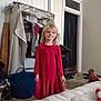 Kensley is registered to the contest to win money with this photo: child, baby, red_dress, blonde_hair, necklace, indoor, carpet, mattress, clothing, furniture, door, laundry_basket, closet, curtain, smile, person, floor, room, household, playful