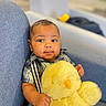 baby, child, plush_toy, yellow, chick, couch, blue, clothing, striped_shirt, face, hand, indoor, cute, soft_toy, smiling, portrait, sitting, infant, furniture, home
