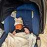 baby, newborn, infant, sleeping, car_seat, stroller, blanket, hat, clothing, harness, safety_buckle, blue, indoors, portrait, resting, child, face, eyes_closed, textile, photography