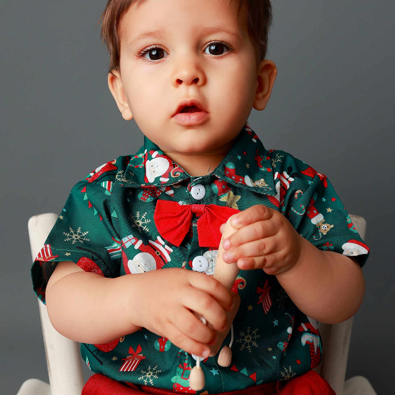 Salvador a rejoint le concours — aidez-le/la à gagner de superbes lots ! background, boy, child, christmas, curious, cute, festive, green_shirt, holiday, indoor, portrait, red_bow, red_pants, sitting, smiling, studio, toddler, white_chair, wooden_toy, young_child