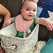 Everly is registered to the contest to win money with this photo: baby, infant, bib, fabric_basket, couch, quilt, arm, hand, smiling, indoor, cozy, blanket, patterned, textile, person, child, cute, happy, seated, closeup