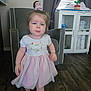 Paisley is registered to the contest to win money with this photo: toddler, child, girl, dress, pink, scrunchie, hair, blue_eyes, indoor, living_room, chair, cabinet, flooring, furniture, person, baby_supplies, curtains, expression, walking, home