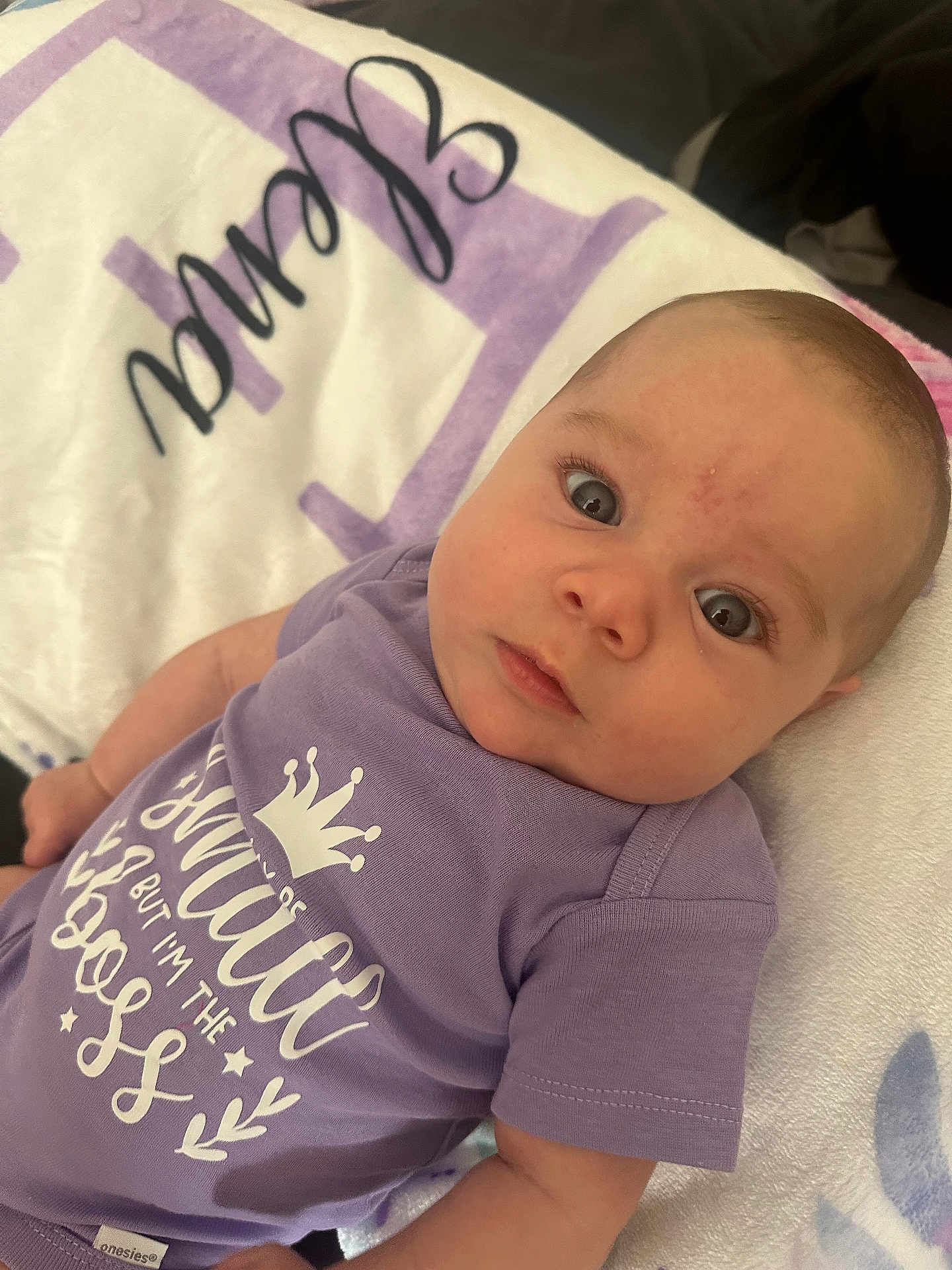 Elena joined the competition — help win amazing prizes! baby, infant, onesie, purple_clothing, blanket, face, eyes, cute, child, soft_texture, lying_down, indoor, expression, young, skin, head, person, apparel, sleepwear, adorable