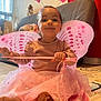 barefoot, butterfly_wings, cat, child, costume, couch, curtains, fairy_costume, floor, happy, headband, home, indoor, person, pink, play_mat, smile, toddler, toy, wand