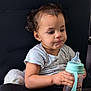 baby_bottle, black_pants, casual_clothing, chair, child, curly_hair, cute, expression, holding, indoor, person, plush_toy, portrait, seat, short_sleeve_shirt, sippy_cup, sitting, toddler, white_toy, young_child