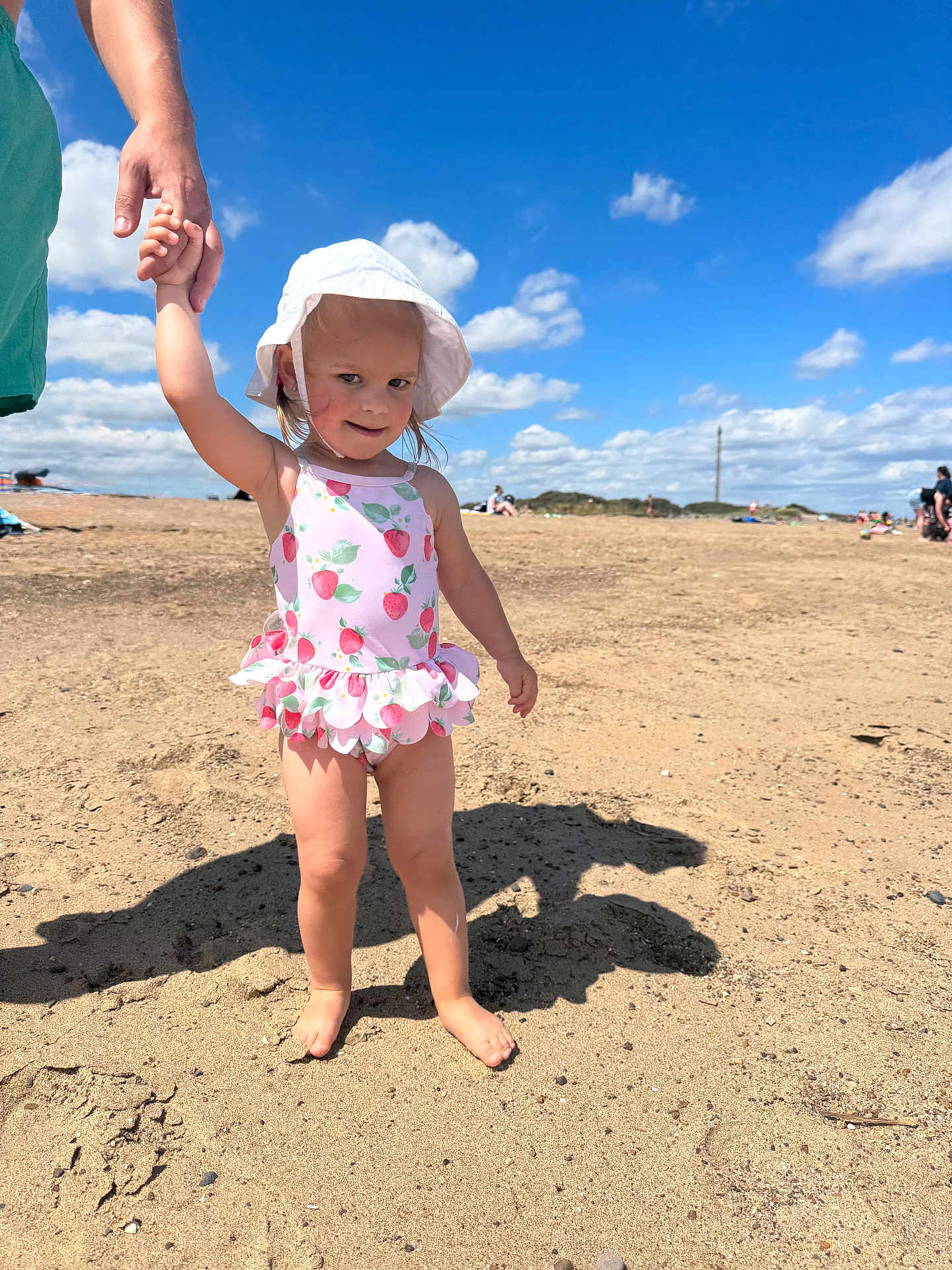 Amelia is registered to the contest to win money with this photo: child, toddler, beach, sand, sunhat, swimsuit, barefoot, holding_hand, adult, blue_sky, clouds, summer, outdoor, sunny, shadow, people, nature, vacation, playful, happy