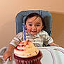 Mateo joined the competition — help win amazing prizes! toddler, child, high_chair, cupcake, birthday_candle, celebration, smile, happy, food, dessert, hand, indoor, clothing, face, person, table, frosting, red_velvet, candle, party