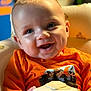 baby, background_blur, blue_eyes, child, close_up, cozy, cup, cute, face, happy, indoor, infant, orange_shirt, person, portrait, sitting, smiling, toy, warm_lighting, young_child