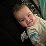 baby, infant, smile, face, pacifier, clothing, dinosaur_print, blanket, lying_down, cute, child, indoors, soft_lighting, closeup, head, person, sleepwear, happy, human, portrait
