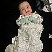 Marcella is registered to the contest to win money with this photo: baby, infant, mittens, sleeping_bag, blanket, pacifier, black_background, lying_down, curious_expression, patterned_clothing, cute, child, portrait, indoor, soft_toys, cozy, small_hands, face, looking_at_camera, comfortable