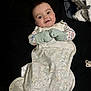 baby, infant, mittens, sleeping_bag, blanket, pacifier, black_background, lying_down, curious_expression, patterned_clothing, cute, child, portrait, indoor, soft_toys, cozy, small_hands, face, looking_at_camera, comfortable