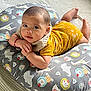 baby, infant, pillow, yellow_clothing, animal_pattern, carpet, cute, child, indoors, portrait, resting, looking_at_camera, colorful, soft_lighting, hand, face, head, floor, laying_down, comfortable