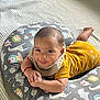 Jason is registered to the contest to win money with this photo: baby, infant, smile, cushion, animal_print, yellow_clothing, bib, hand, face, lying_down, soft_texture, knitted_blanket, cute, child, indoors, happy, person, portrait, baby_girl_or_boy, playful
