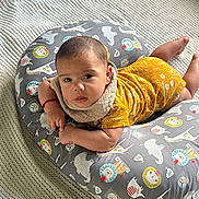 Jason is registered to the contest to win money with this photo: baby, child, infant, cushion, animal_print, yellow_clothing, bib, knitted_blanket, lying_down, curious, face, indoors, cute, resting, soft_texture, colorful, person, toddler, portrait, young