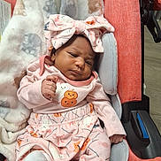 Kyra'Yana is registered to the contest to win money with this photo: baby, infant, child, portrait, stroller, pink_clothing, bow_headband, pumpkin_pattern, blanket, seated, indoors, cozy, face, eyes, hands, smiling, newborn, baby_clothes, cushion, photography