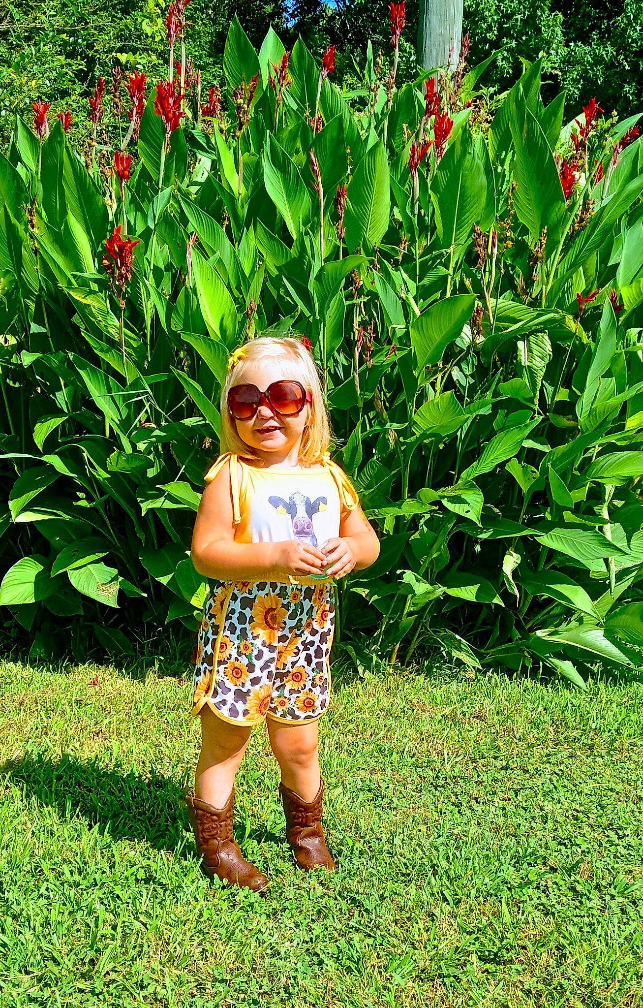 Annie is registered to the contest to win money with this photo: baby_toddler_clothing, botany, eyewear, flower, garden, glasses, grass, grass_family, grassland, groundcover, happy, lawn, meadow, people_in_nature, person, plant, shorts, shrub, smile, sunglasses