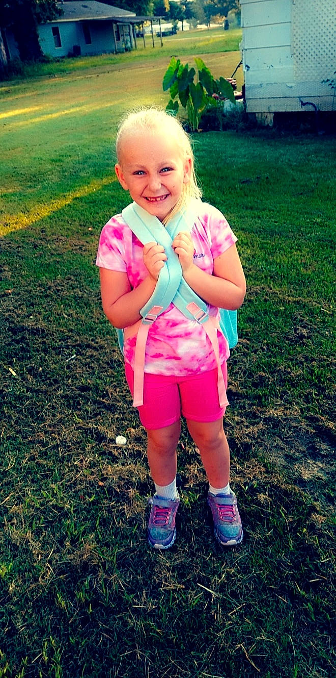 Angela is registered to the contest to win money with this photo: arm, baby_toddler_clothing, face, fun, gesture, grass, hair, happy, head, joy, leg, people_in_nature, person, pink, plant, shorts, smile, sneakers, summer, sunlight