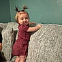 toddler, child, standing, couch, indoor, smiling, hair_pigtails, pink_socks, dress, gray_couch, wall, person, happy, furniture, home, playful, infant, young_child, cute, portrait