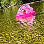 child, toddler, inflatable_boat, pink, water, river, rocks, nature, trees, outdoor, sunlight, reflection, canopy, floating, baby, playful, summer, daylight, person, recreation