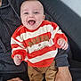adult_hand, baby, casual_clothing, child, couch, happy, home, human, indoor, infant, joyful, orange, pants, person, portrait, seated, smiling, socks, striped_clothing, sweater