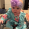 baby, child, headband, flower, floral_clothing, sitting, blanket, indoor, cute, curious, sock, portrait, infant, person, blue_clothing, pink_flower, soft_lighting, furniture, cabinet, home