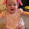 Sofia is registered to the contest to win money with this photo: baby, child, smiling, pink, headband, bunny_ears, dress, sitting, indoor, toy, furniture, happy, cute, infant, person, floor, playful, patterned_surface, arms_outstretched, room