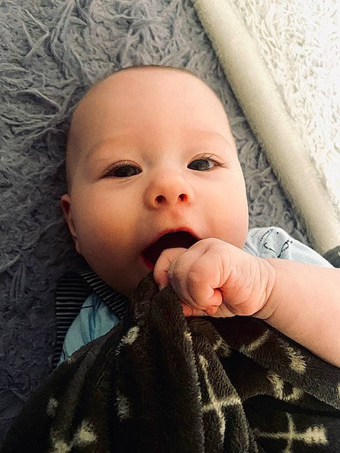 Harlen is registered to the contest to win money with this photo: baby, baby_toddler_clothing, cheek, comfort, eye, eyelash, finger, gesture, hand, happy, iris, linens, lip, mouth, nail, nose, person, skin, sleeve, thumb