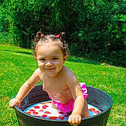 Olivianna is registered to the contest to win money with this photo: child, toddler, milk, strawberries, tub, outdoor, grass, greenery, sunlight, pink_clothing, curly_hair, pigtails, smiling, playful, summer, nature, water, baby, candid, fun