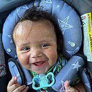 Donovan is registered to the contest to win money with this photo: baby, smiling, car_seat, pacifier, star_pattern, child, happy, infant, clothing, seatbelt, face, hand, cute, young_child, safety, indoors, person, closeup, expression, red_bracelet