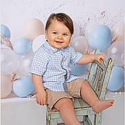 Charlie is registered to the contest to win money with this photo: toddler, child, smile, blue_eyes, checkered_shirt, beige_shorts, wooden_chair, pastel_colors, balloons, birthday_theme, studio_photo, indoor, cute, happy, baby, portrait, sitting, playful, light_background, rustic_furniture