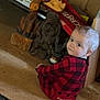 animal_figures, baby, blue_eyes, carpet, checkered_pattern, child, cozy, curious, face, floor, head, indoor, looking_back, pajamas, red_clothing, scrabble_box, sitting, toy, wood_paneling, wooden_carvings